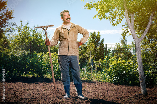 Farmer working in the garden with the help of a rake leveling plowed land, on a sunny day