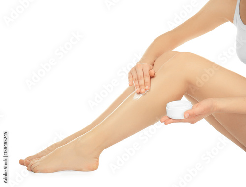 Woman applying cream onto her legs on white background