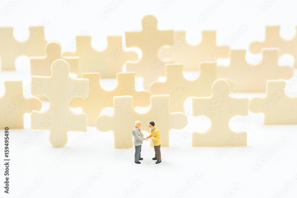 business miniature people shaking hands on jigsaw puzzle pieces background