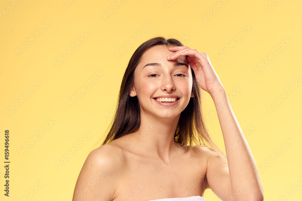 Woman with a smiling hand touched her face on a yellow background
