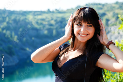 Prtty cheerful young woman listening to music in headphones outdoors. photo