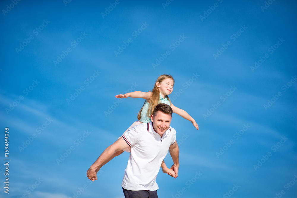 Dad and little girl daughter playing on the beach, fly, run, laugh at the blue sky background Dad and little girl daughter playing on the beach, fly, run, laugh at the blue sky background