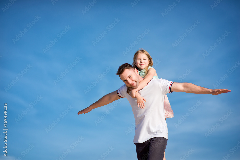 Dad and little girl daughter playing on the beach, fly, run, laugh at the blue sky background Dad and little girl daughter playing on the beach, fly, run, laugh at the blue sky background