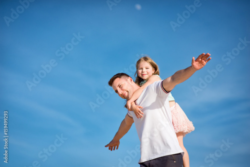 Dad and little girl daughter playing on the beach, fly, run, laugh at the blue sky background