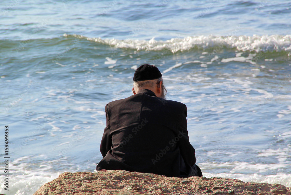 Religious Jew sitting on the coast of Mediterranean sea in Israel and watching the waves, deep in thought. Religious Jew sitting on the coast of Mediterranean sea in Israel and watching the waves, deep in thought.