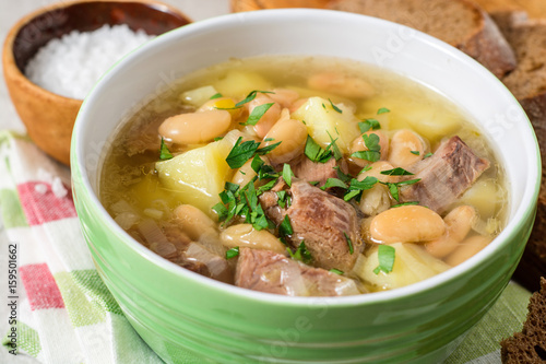 Beef soup with potatoes, beans and leeks in ceramic bowl on stone background.