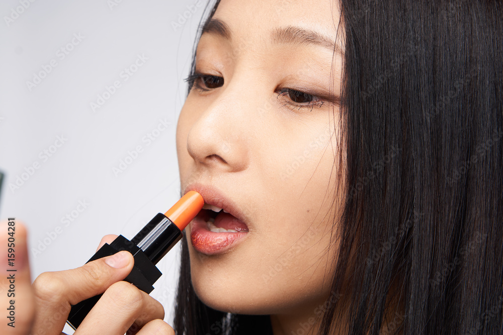 Woman paints lips, woman looks in mirror on light background portrait Woman paints lips, woman looks in mirror on light background portrait