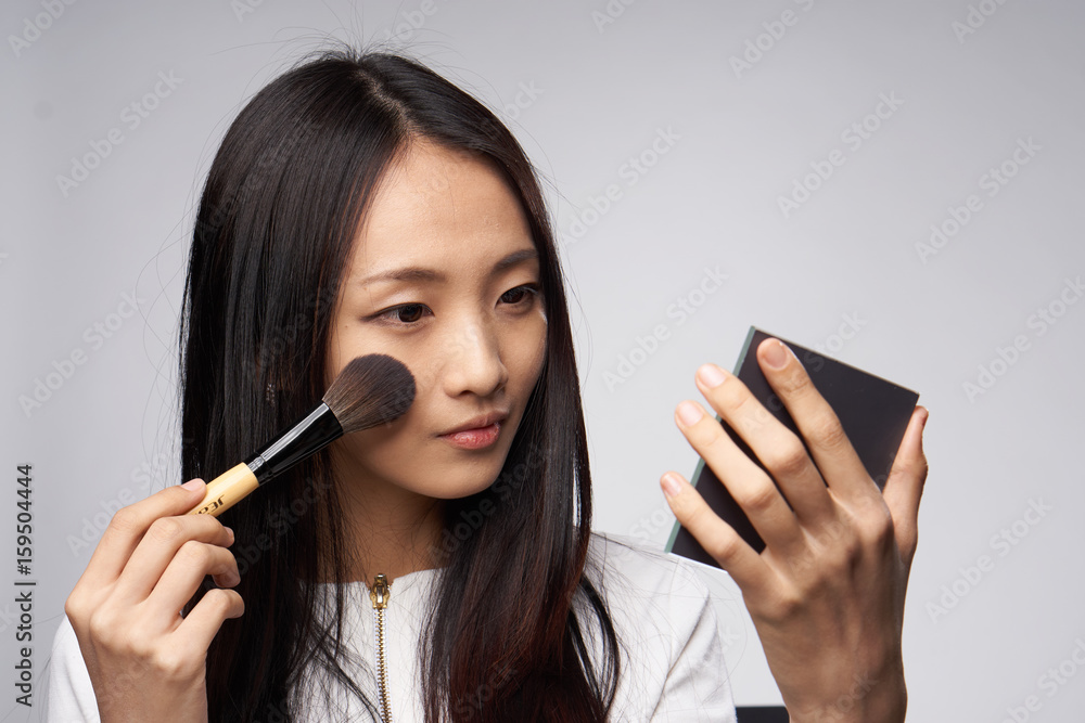 Woman pores herself, woman with a cosmetic brush and with a mirror on a gray background Woman pores herself, woman with a cosmetic brush and with a mirror on a gray background