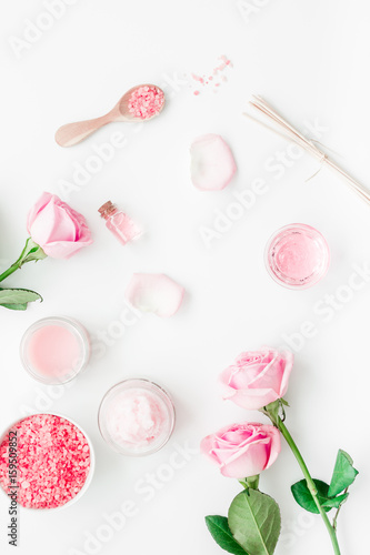 cosmetic set with rose blossom and body cream on white desk background top view