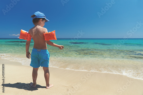 Boy in floating sleeves on a beach with transparent water.