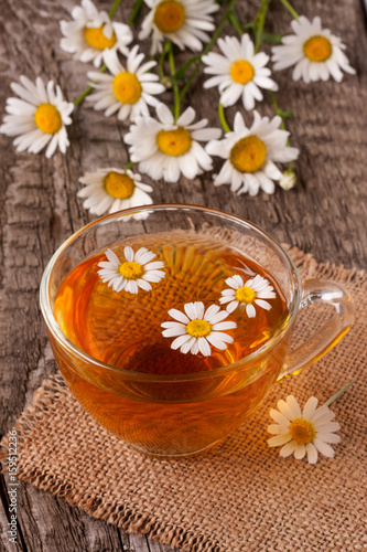 Herbal tea with fresh chamomile flowers on old wooden background