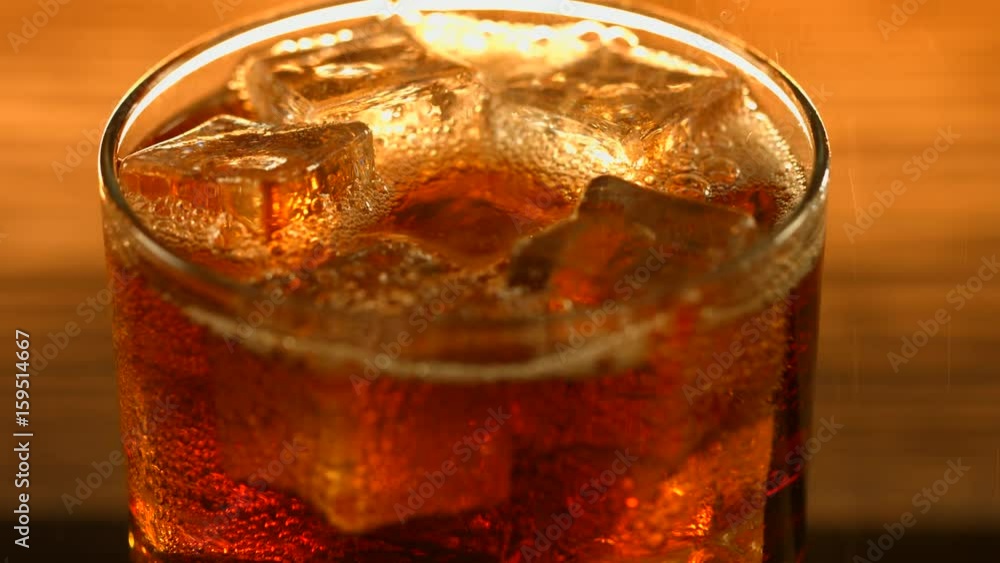 Cola pouring in glass with ice cubes over wooden table background. 4K UHD video 3840X2160p Cola pouring in glass with ice cubes over wooden table background. 4K UHD video 3840X2160p