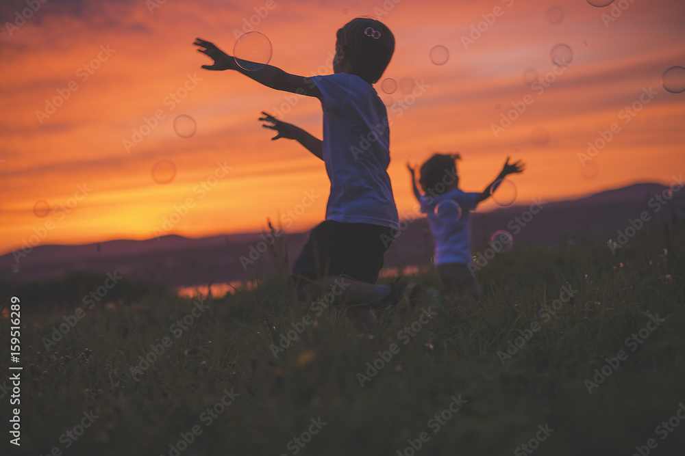 boys running to hit bubble on a sunset meadow