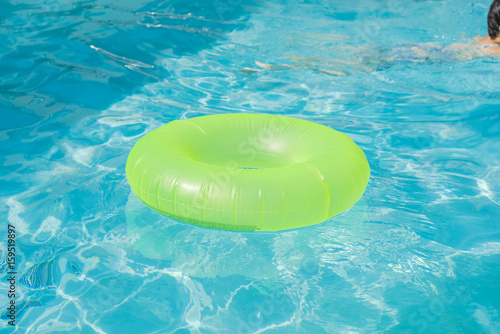 Bright green float in blue swimming pool, ring floating in a refreshing blue swimming pool with waves reflecting in the summer sun. Active vacation background. Lifesaver for kid. Sunny day at the pool
