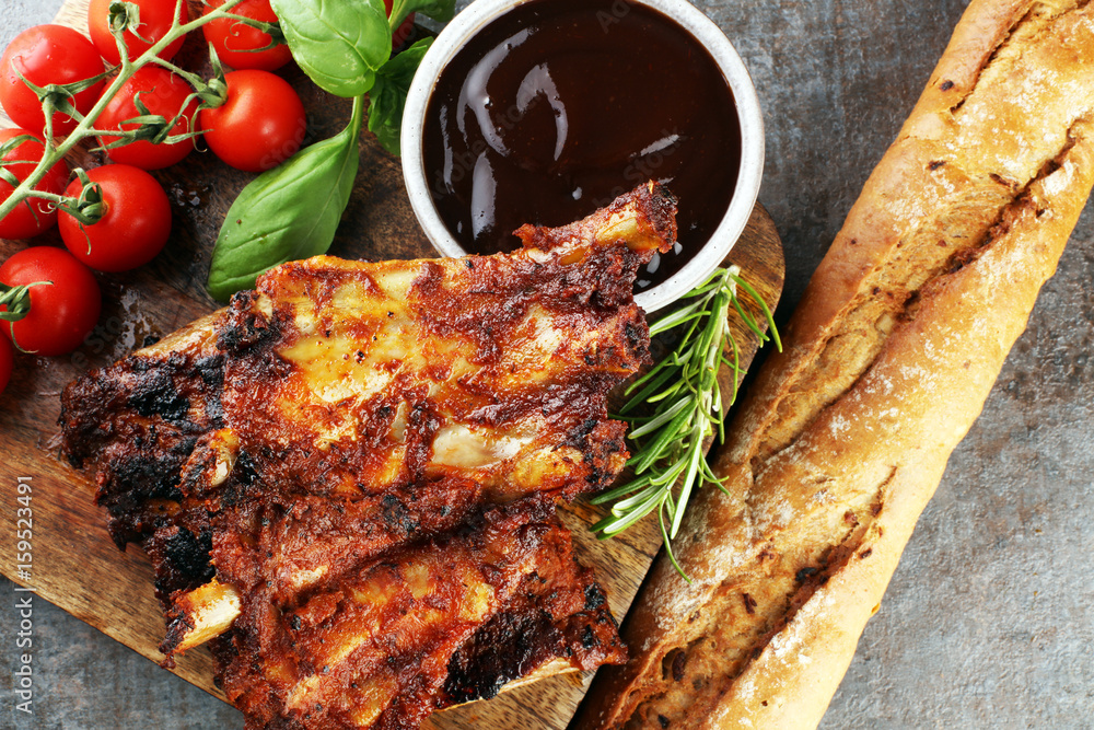 Spicy hot grilled spare ribs from a summer BBQ served with fresh tomatoes on an old vintage wooden cutting board