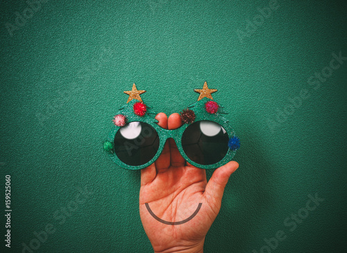 Christmas glasses that decoration with Christmas tree and red ball on hand on green background