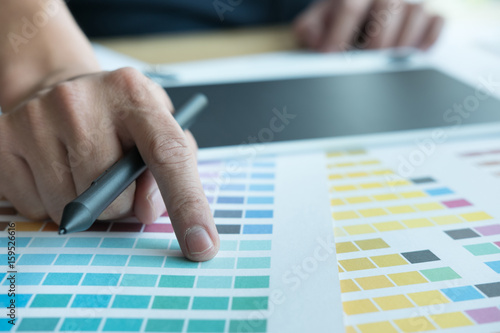 young graphic designer working with color swatch. creative man using stylus pen and digital tablet at modern office.  Architect drawing with work tools and sample colour catalog. 