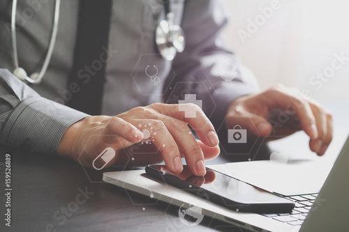 close up of smart medical doctor working with mobile phone and laptop computer and stethoscope on dark wooden desk