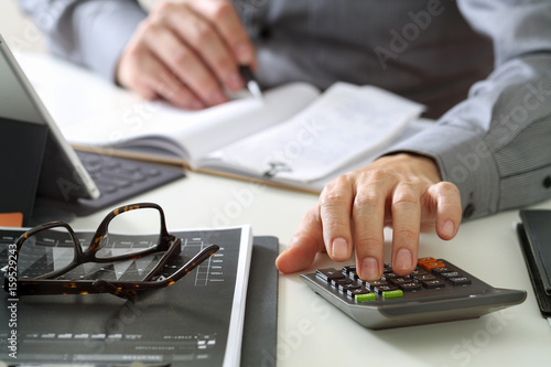 businessman hand working with finances about cost and calculator and latop with mobile phone on withe desk in modern office