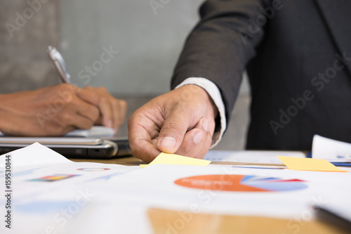 young successful man holding sticky note paper on meeting in modern office interior Businessman brainstorming, make a business plan, working on table with financial and marketing graph chart