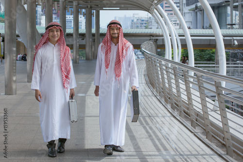 two arabian businessman with briefcase and walk together around modern city