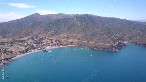 Wallpaper Mural Slow forward moving aerial shot approaching a harbor town with a sandy beach and hills overlooking the town. Boats moored, with palm trees throughout the town. A boat travels to the right. Torontodigital.ca