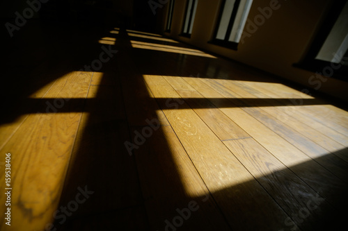 Window frames cast shadows on the floor of a wide empty room