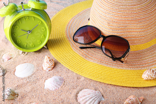Green alarm clock with sunglasses and hat on beach sand