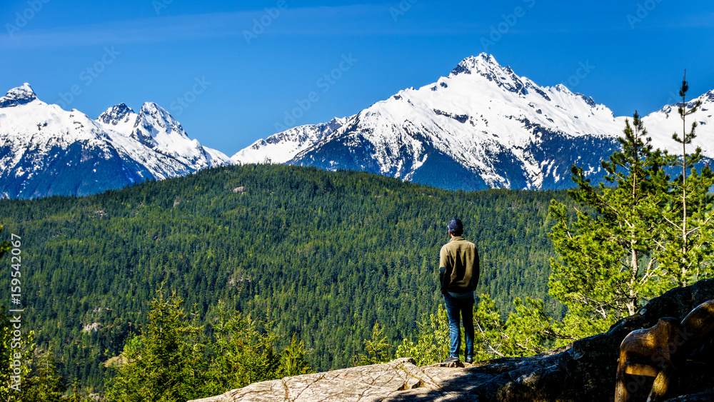 Man looking at the Tantalus Mountain Range with snow covered peaks of Alpha Mountain, Serratus and Tantalus Mountain, seen from a viewpoint along the Sea to Sky Highway between Squamish and Whistler