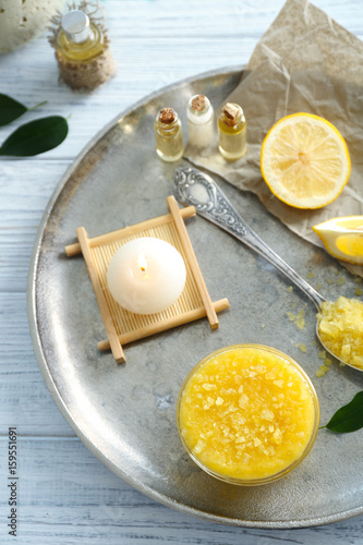 Glass bowl with lemon scrub, candle, bottles of oil and sea salt on metal tray
