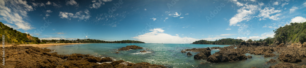 Panorama of a sandy beach with volcanic stones and turquoise sea in New Zealand