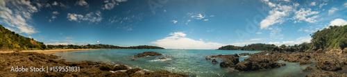 Panorama of a sandy beach with volcanic stones and turquoise sea in New Zealand
