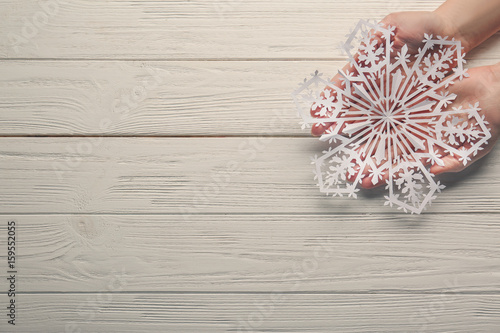 Female hands with beautiful paper snowflake on light wooden background