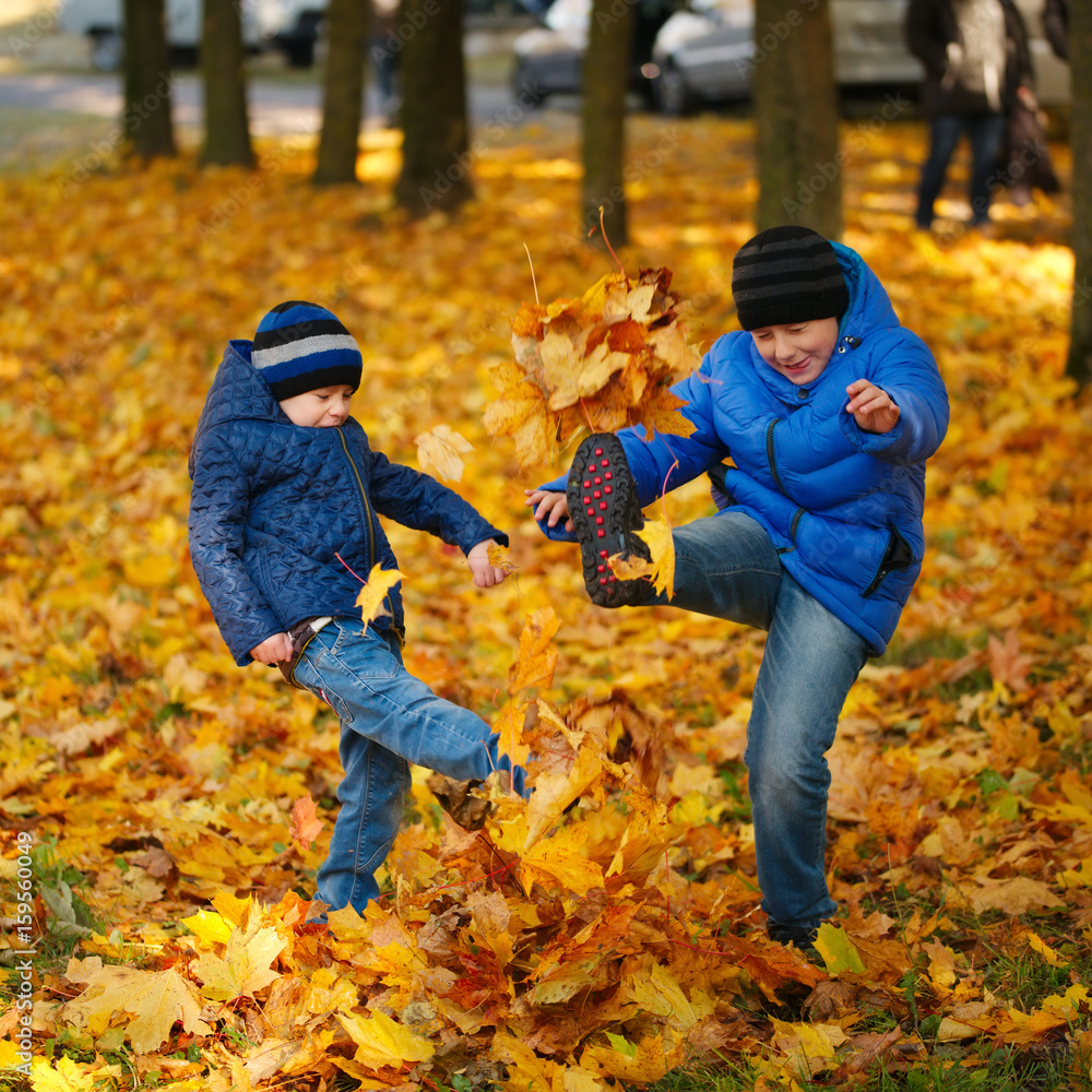 two boys kick maple leaves in park two boys kick maple leaves in park