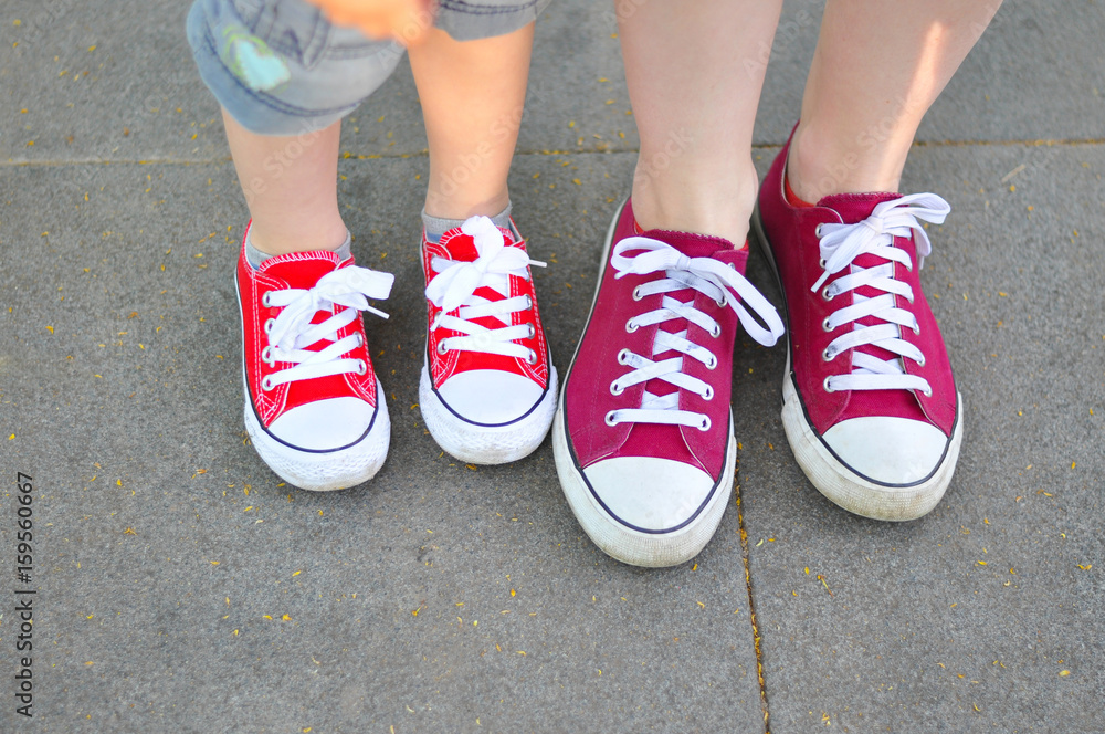 Legs of a boy and his mom red shoes on the street asphalt. Big and small feets in red sneakers 