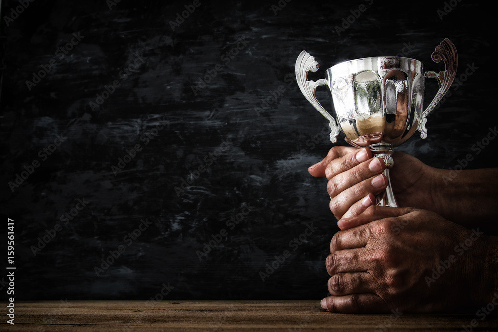 low key image of a man holding a trophy cup over dark background
