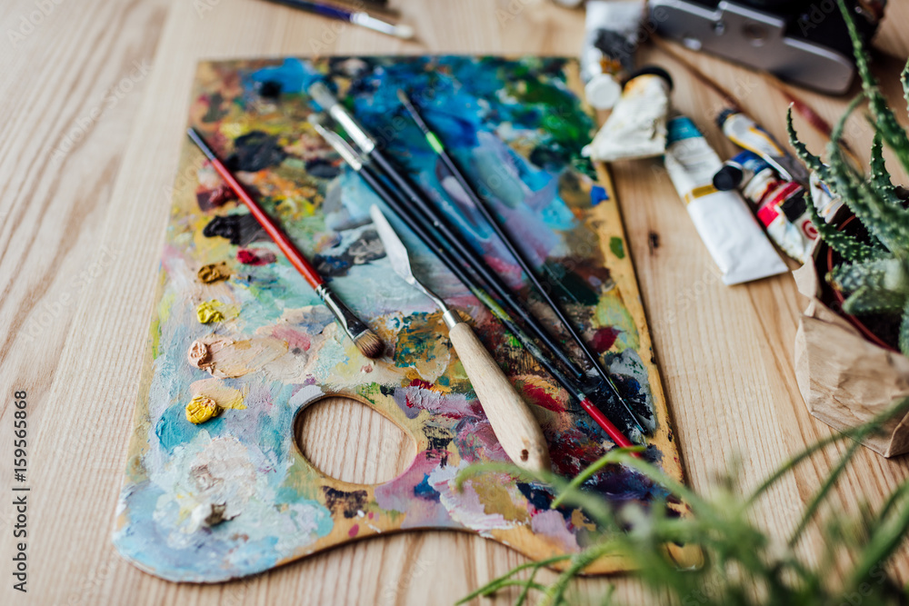 High angle view of artist palette with paint brushes, palette knife and oil paint tubes on the table