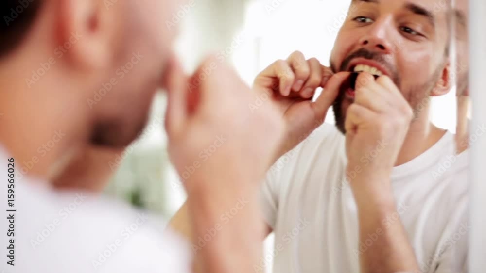 man with dental floss cleaning teeth at bathroom man with dental floss cleaning teeth at bathroom