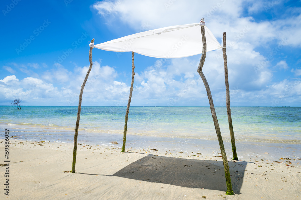 Rustic sun shade made from a sheet strung from sticks stands on an empty beach in Bahia, Brazil Rustic sun shade made from a sheet strung from sticks stands on an empty beach in Bahia, Brazil