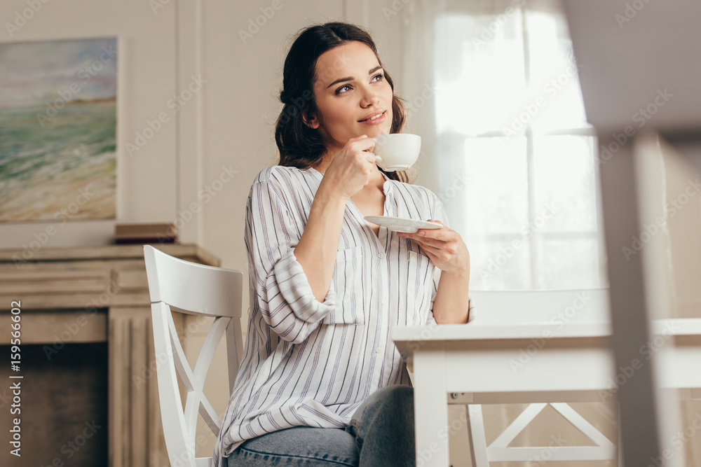 pensive young woman drinking coffee while sitting at table at home pensive young woman drinking coffee while sitting at table at home