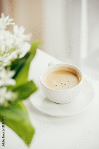 close up of cup of coffee with bouquet of flowers on white tabletop