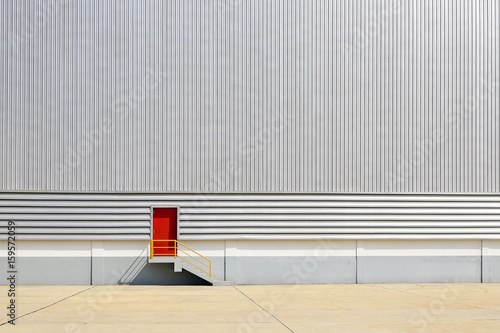 The red exit door at the sheet metal wall of factory building.
