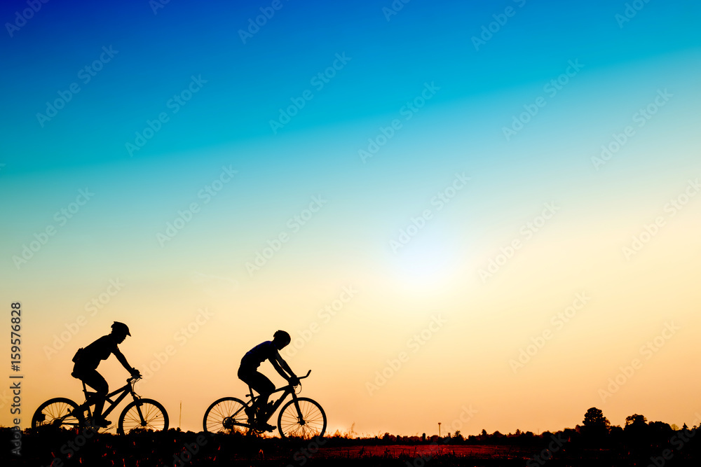 Obraz premium Silhouette of cyclists riding bikes on road at sunset.