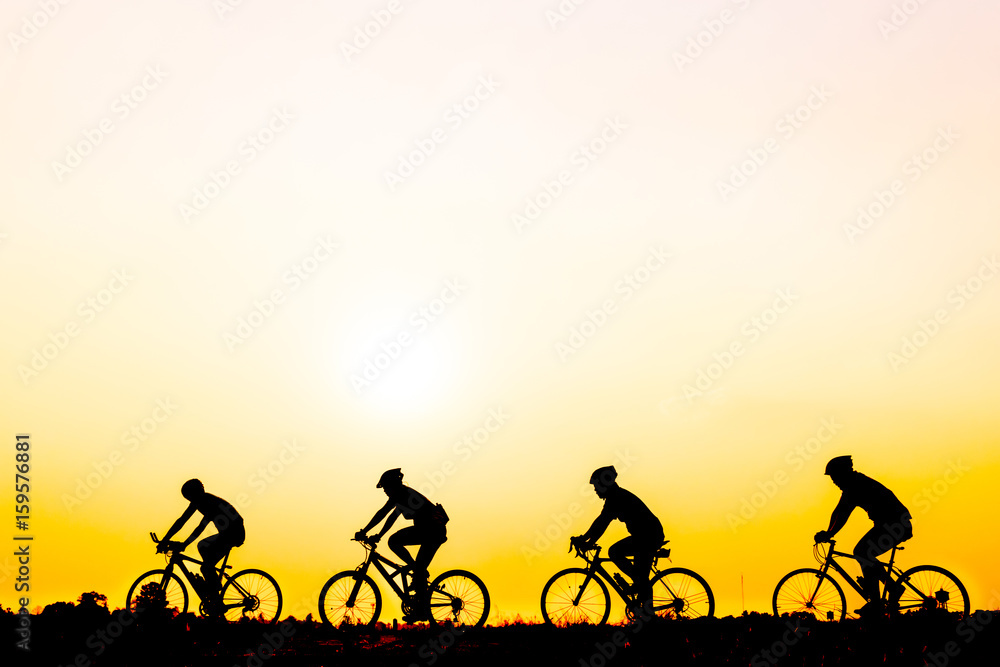Obraz premium Silhouette of cyclists riding bikes on road at sunset.