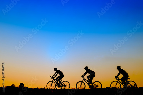 Silhouette of cyclists riding   bikes  on road at sunset.