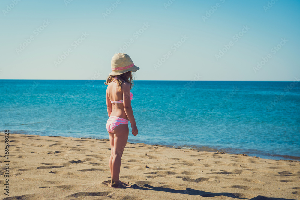 little girl in swimsuit and hat standing on the beach