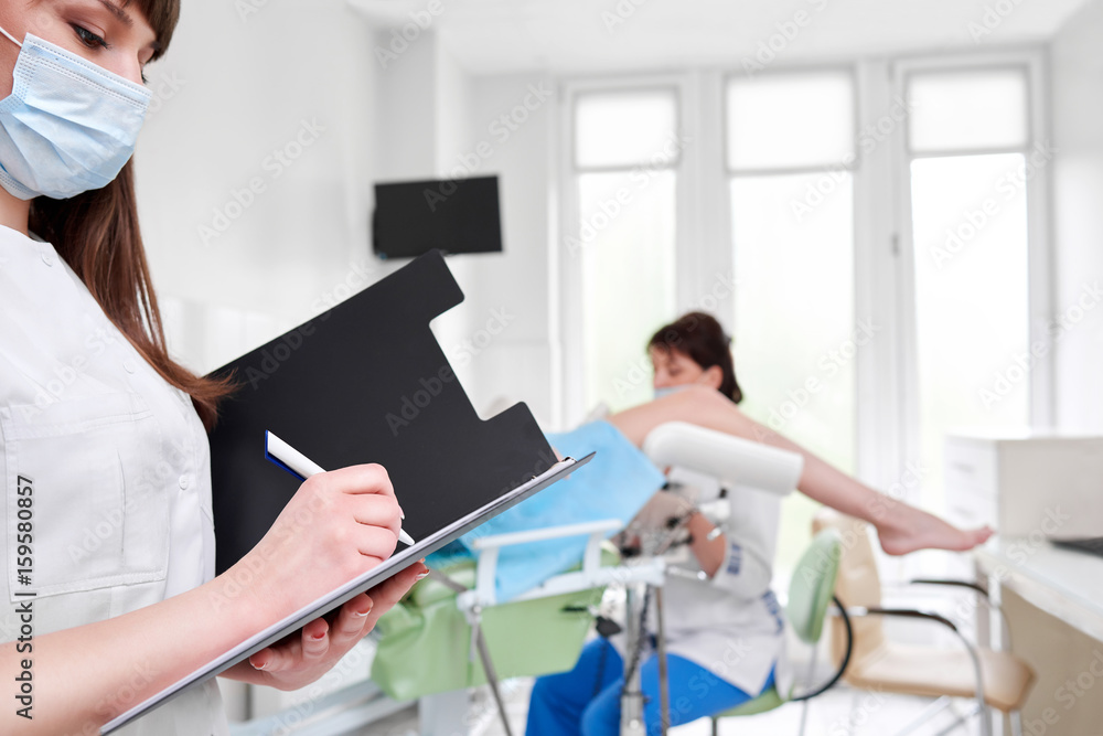 Obraz premium Cropped shot of a nurse writing on her clipboard professional gynecologist examining her patient on the gynecological chair on the background copyspace medicine gynecology health concept.
