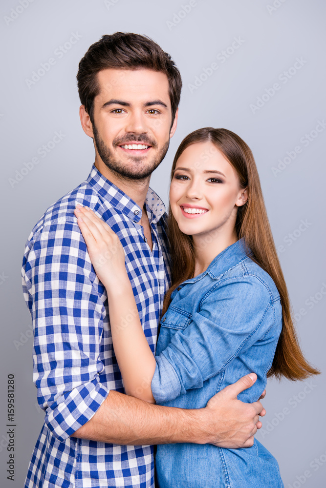 True love, trust, friendship, happiness. Two young cute lovers are looking at the camera and smile, wearing casual outfits, hugging gently on the pure background True love, trust, friendship, happiness. Two young cute lovers are looking at the camera and smile, wearing casual outfits, hugging gently on the pure background