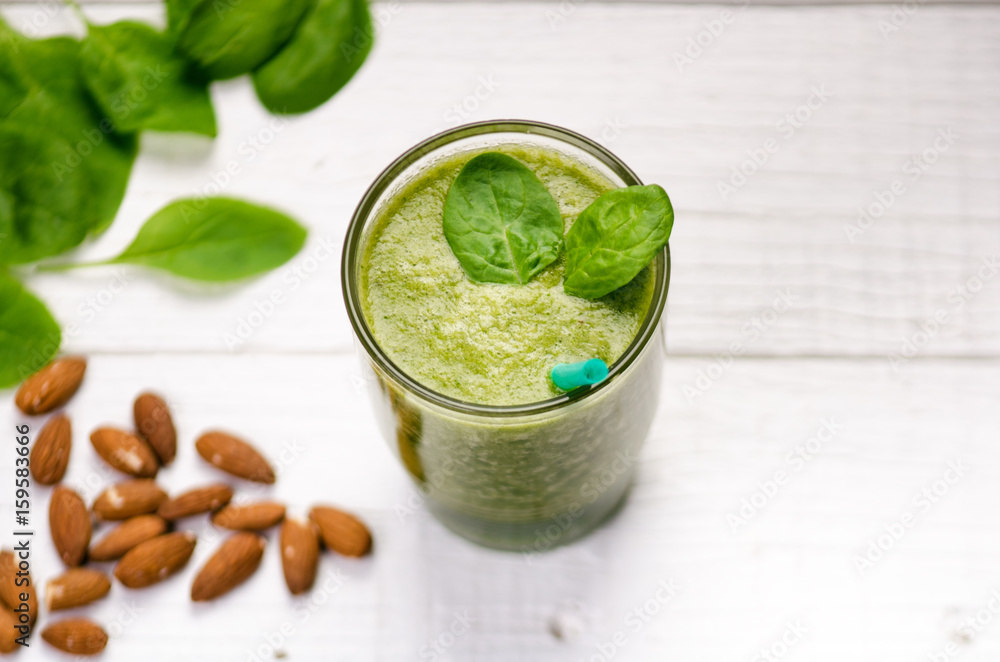 Spinach smoothie on a wooden white background. Glass of smoothie with two leaves of spinach. Nuts. Healthy food. Breakfast. Spinach smoothie on a wooden white background. Glass of smoothie with two leaves of spinach. Nuts. Healthy food. Breakfast.