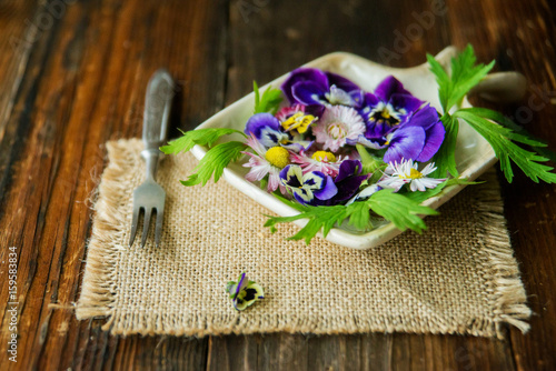 Fresh salad with smoked salmon, black olives, cherry tomatoes and edible flowers on wooden background.